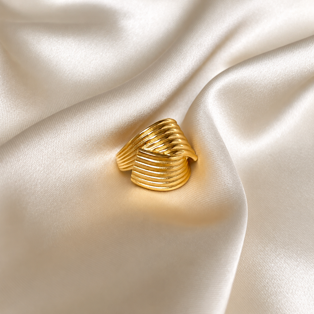 Hedda Huggie Ring i guld fotograferad på ljust silkestyg. Vattentåligt och allergivänligt smycke i rostfritt stål med 18K PVD-guldplätering från Alora Avenue.