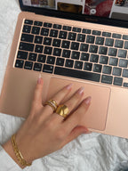 Hedda Huggie Ring från Alora Avenue – en bred, guldig statementring med strukturerad yta. Här stylad på handen framför en rosa MacBook Air.
