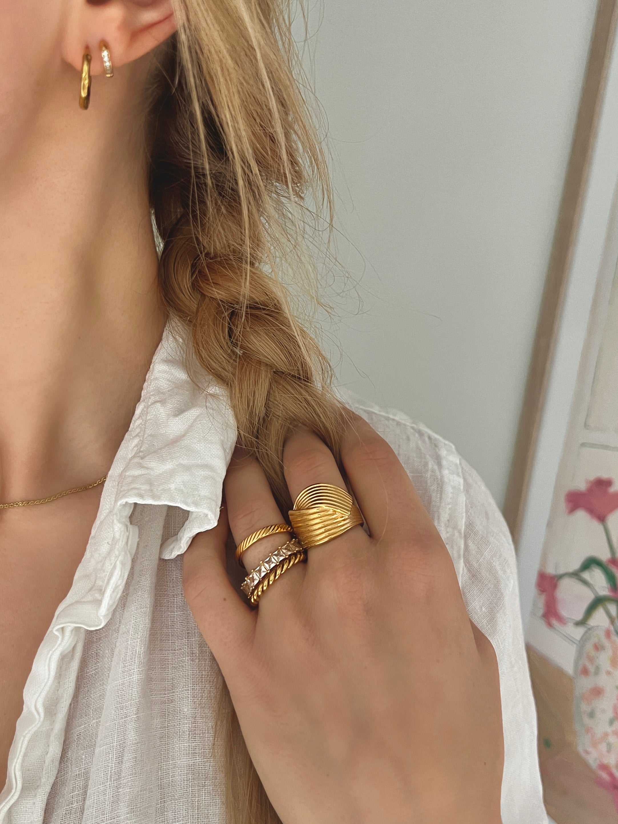 Hedda Huggie Ring från Alora Avenue – bred, guldig statementring med räfflad yta. Stylad med flätat hår och vit linneskjorta för en somrig look.