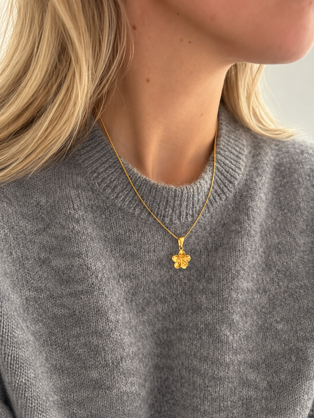 Hibiscus Floral Pendant – Blumenförmiger Anhänger in Gold an einer dünnen Kette, getragen von einem Model. Wasserfester Goldschmuck von Alora Avenue.