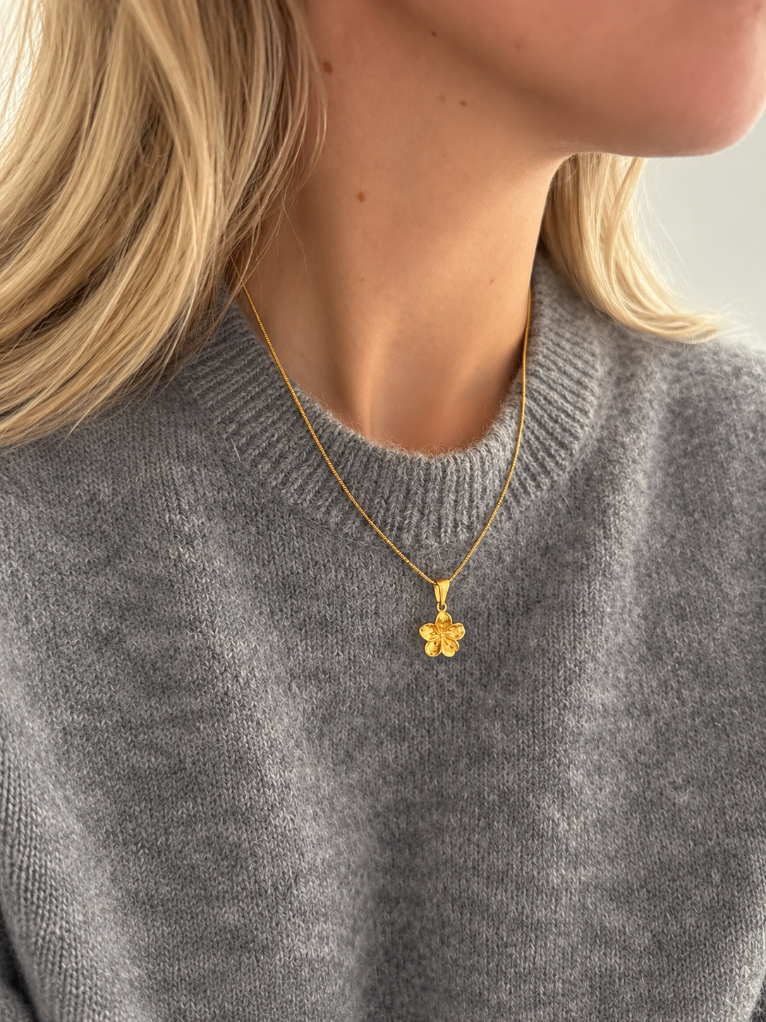 Hibiscus Floral Pendant – blomformat hänge i guld på tunn kedja, buret av modell. Vattentåligt guldsmycke från Alora Avenue.