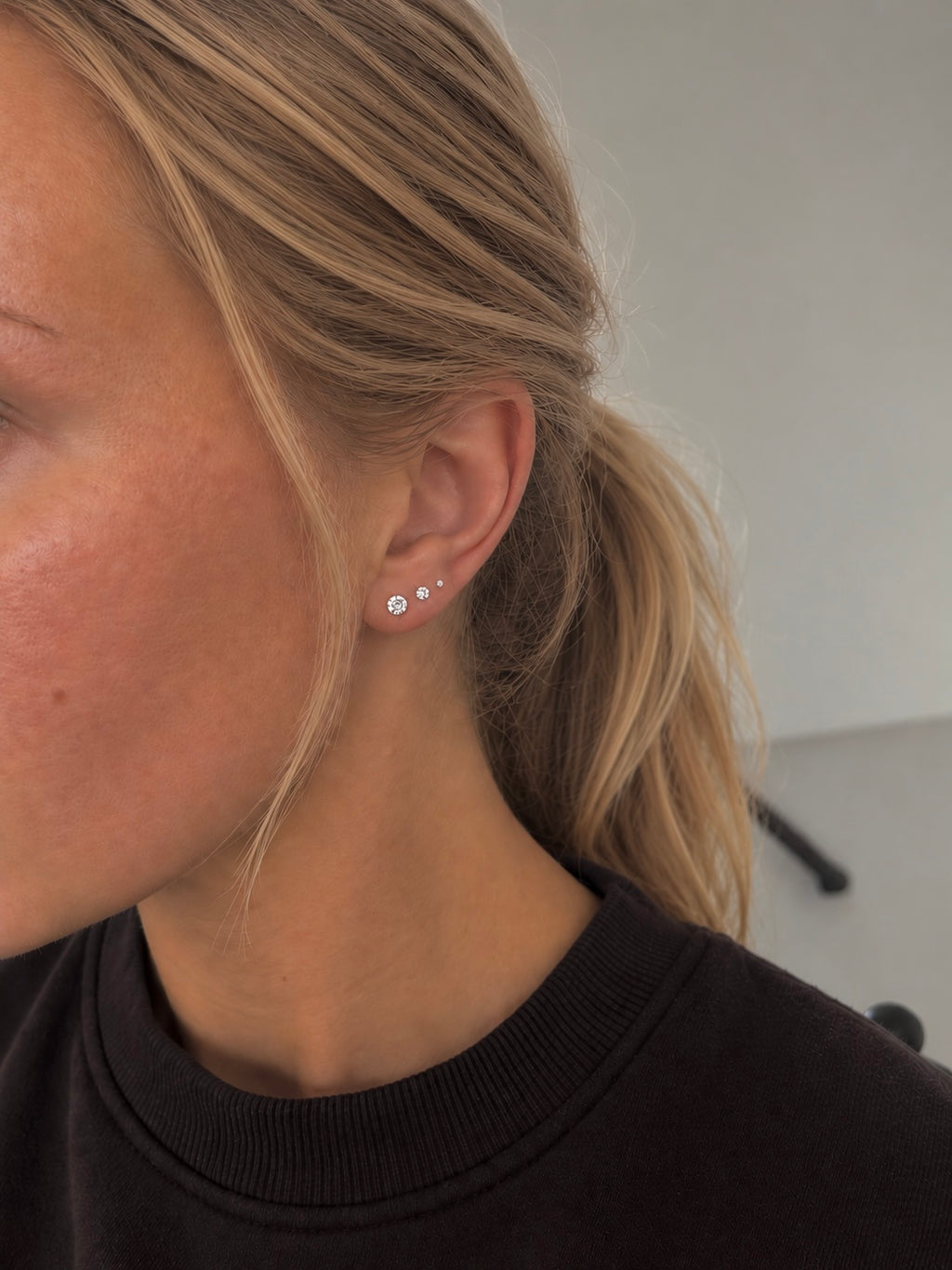 Iris örhängen i silver burna på modell – tre glittrande kristallstuds i storlekarna 2, 3 och 4 mm sittande i rad längs örat. Vattentåliga studs i kirurgiskt stål från Alora Avenue.