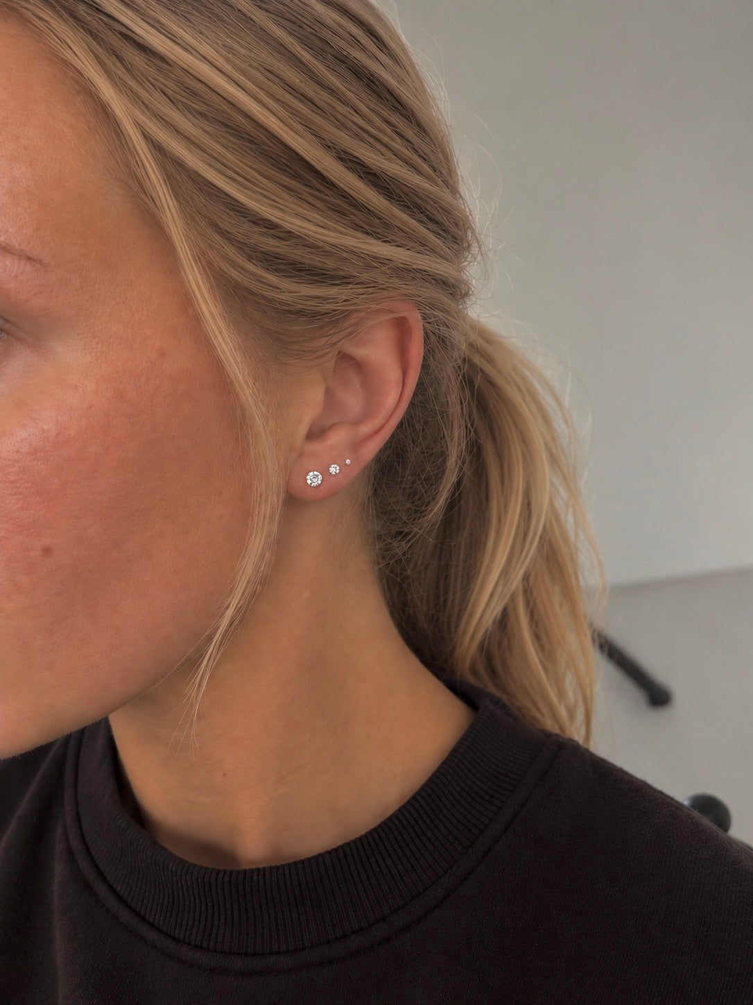 Iris örhängen i silver burna på modell – tre glittrande kristallstuds i storlekarna 2, 3 och 4 mm sittande i rad längs örat. Vattentåliga studs i kirurgiskt stål från Alora Avenue.