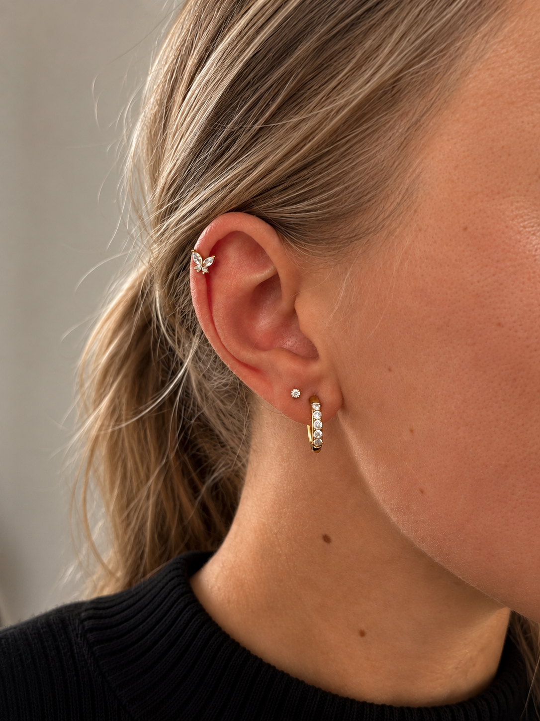Guldörhängen på modell i stacked look – Iris Star Stud, Anni Aura Hoops och Bella Butterfly Stud kombinerade. Vattentåliga, allergivänliga örhängen från Alora Avenue.