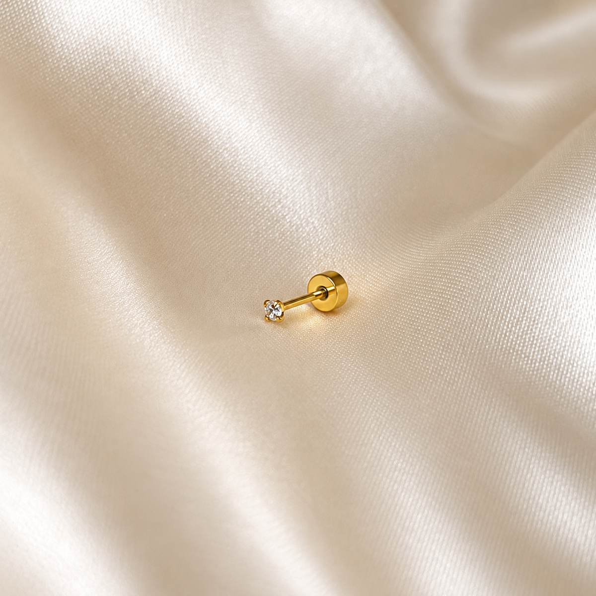 Iris Star Stud i guld, närbild på ett enskilt stift mot ljust silkestyg. Vattentåligt och allergivänligt örhänge i rostfritt stål med 18K PVD-guldplätering från Alora Avenue.