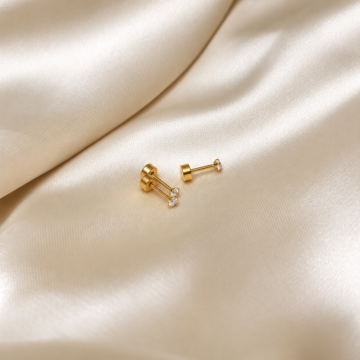 Iris Star Stud i guld, ett par stift fotograferade på ljust silkestyg. Vattentåliga och allergivänliga örhängen i rostfritt stål med 18K PVD-guldplätering från Alora Avenue.