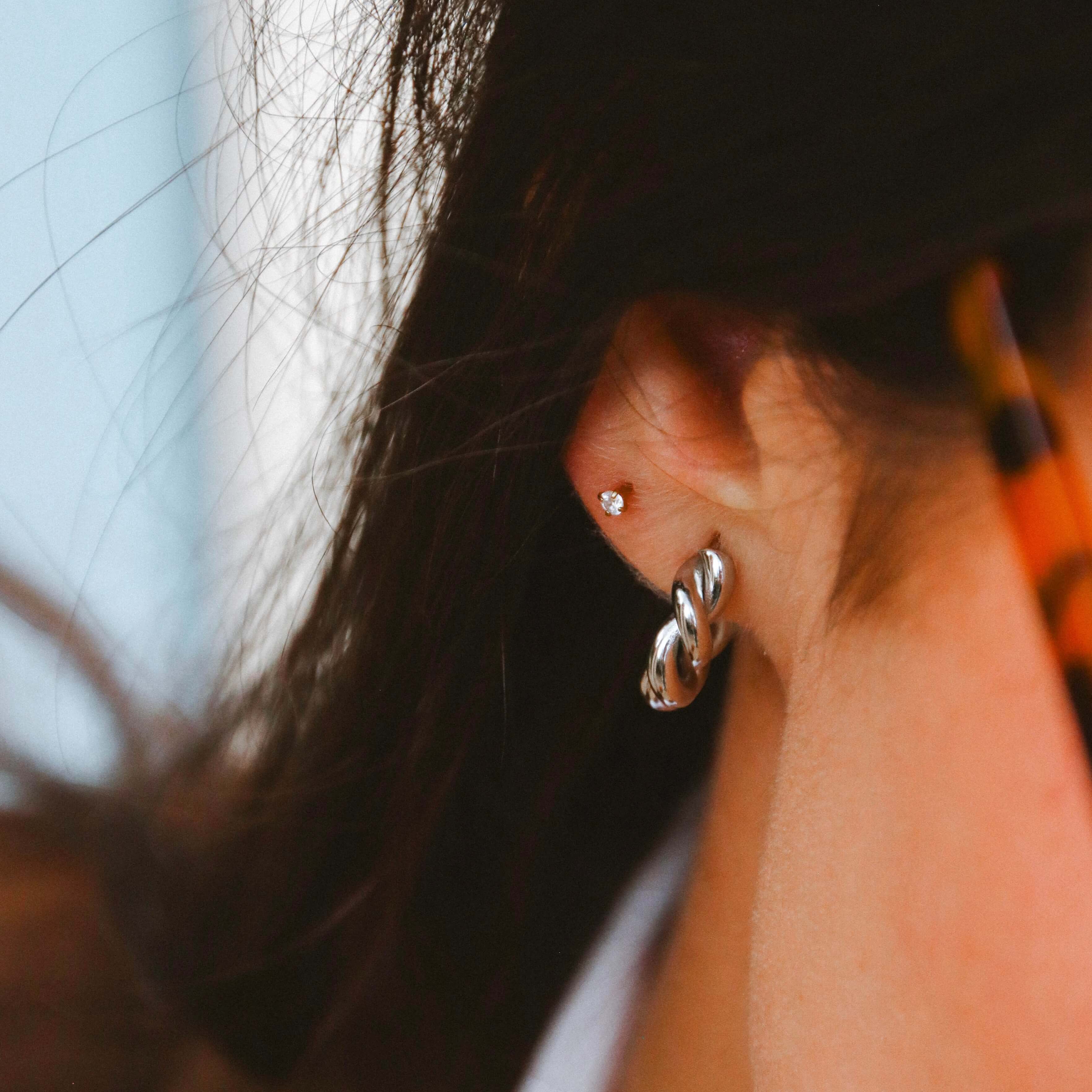 Iris Star Stud i guld med vit sten stylad i en elegant ear stack på kvinna med skinnjacka. Diskret och lyxig liten stud från Alora Avenue – perfekt för vardag och fest.