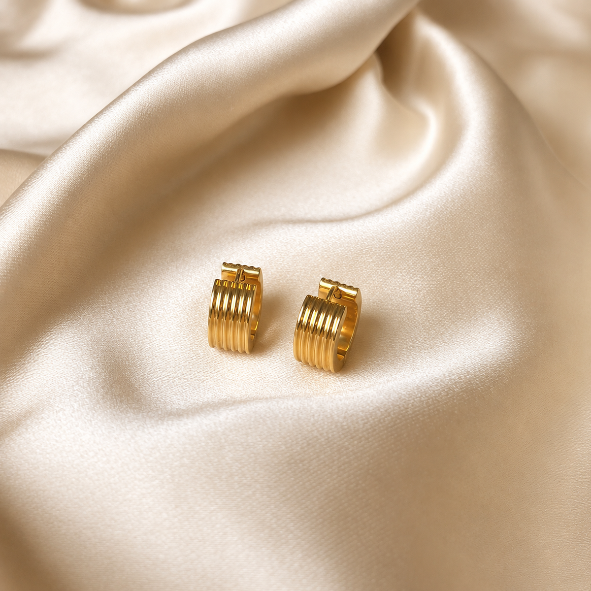 Kairo Vintage Hoops i guld fotograferade på ljust silkestyg. Vattentåliga och allergivänliga örhängen i rostfritt stål med 18K PVD-guldplätering från Alora Avenue.