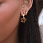 Lily Lace Loop – guldigt blomformat örhänge i rostfritt stål, fotograferat på modell. Vattentåligt och allergivänligt smycke från Alora Avenue.