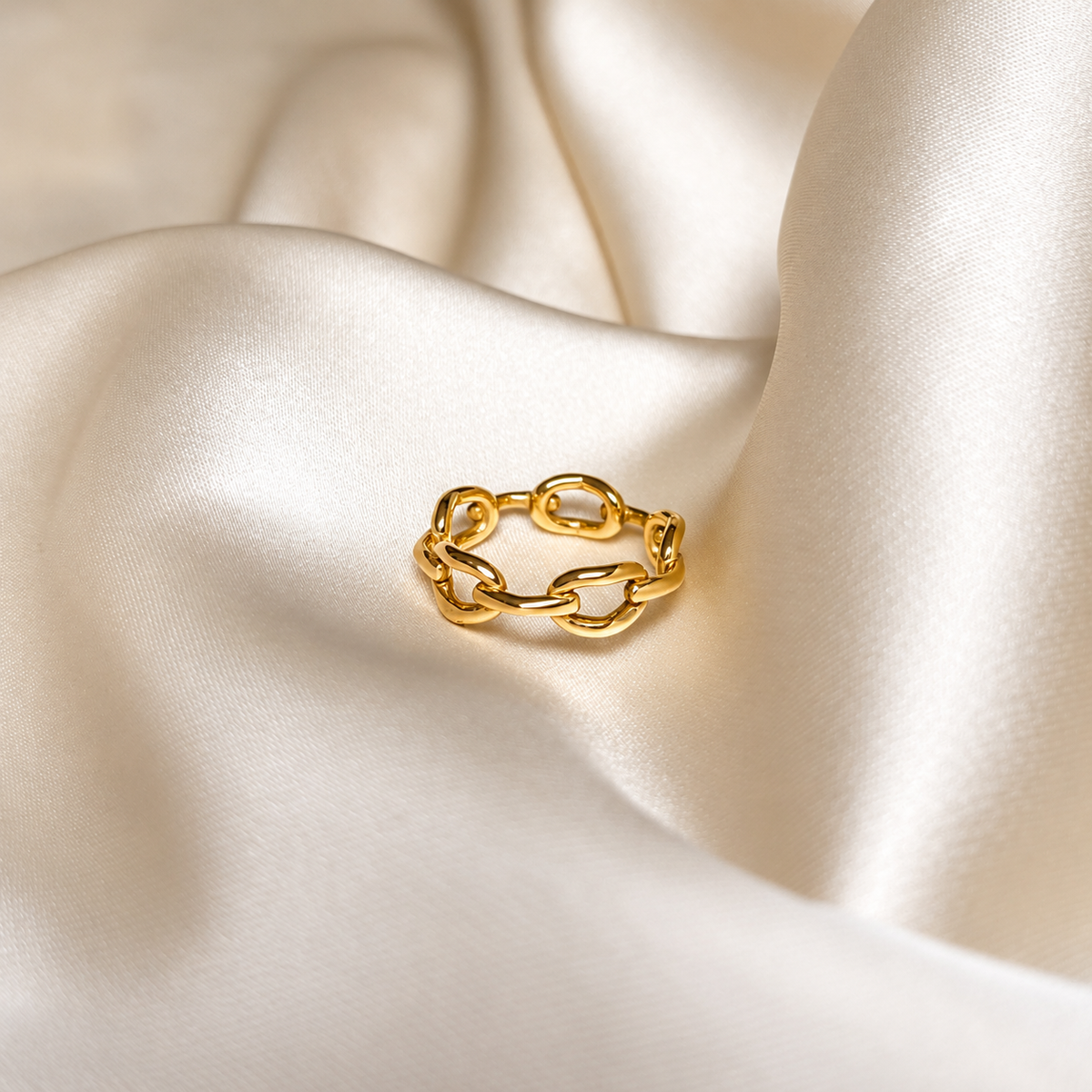 Lina Link Ring i guld fotograferad på ljust silkestyg. Vattentåligt och allergivänligt smycke i rostfritt stål med 18K PVD-guldplätering från Alora Avenue.
