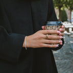 Livia Loop Ring i guld stylad på hand som håller en kaffekopp. Elegant flätad ring från Alora Avenue – vattentålig, allergivänlig och tidlös i designen.