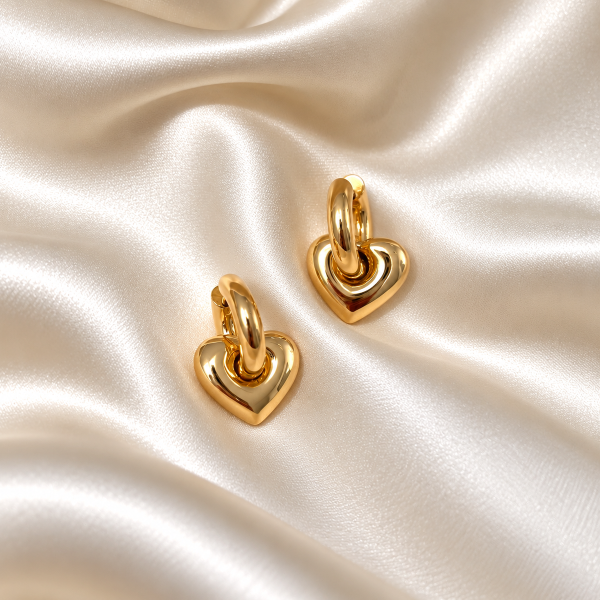 Lova Love Loops i guld fotograferad på ljust silkestyg. Vattentåligt och allergivänligt smycke i rostfritt stål med 18K PVD-guldplätering från Alora Avenue.