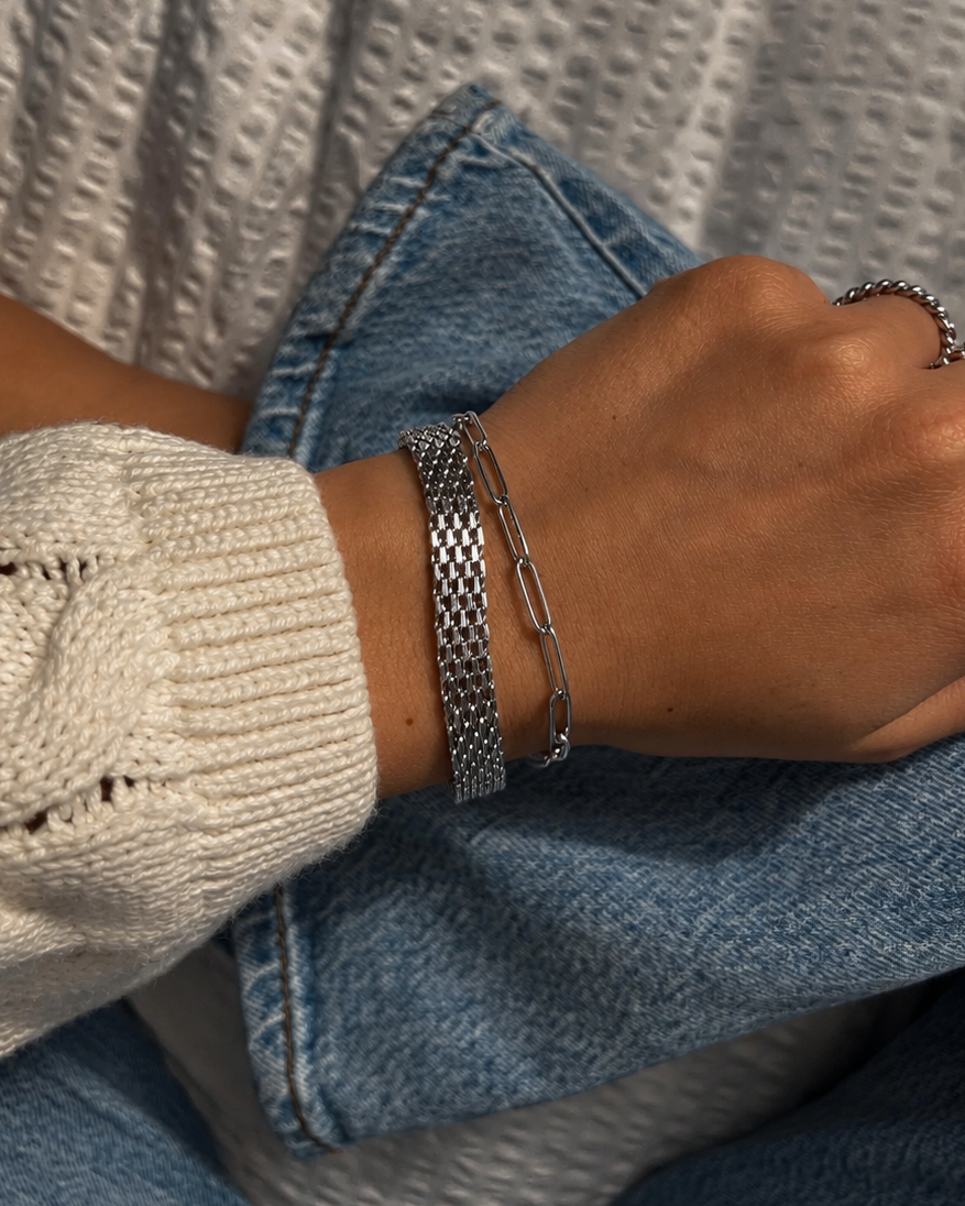 Lucid Clip Bracelet i silver på modell mot denim, buret i en stack med fler silverarmband. Vattentåligt och allergivänligt armband i rostfritt stål från Alora Avenue.