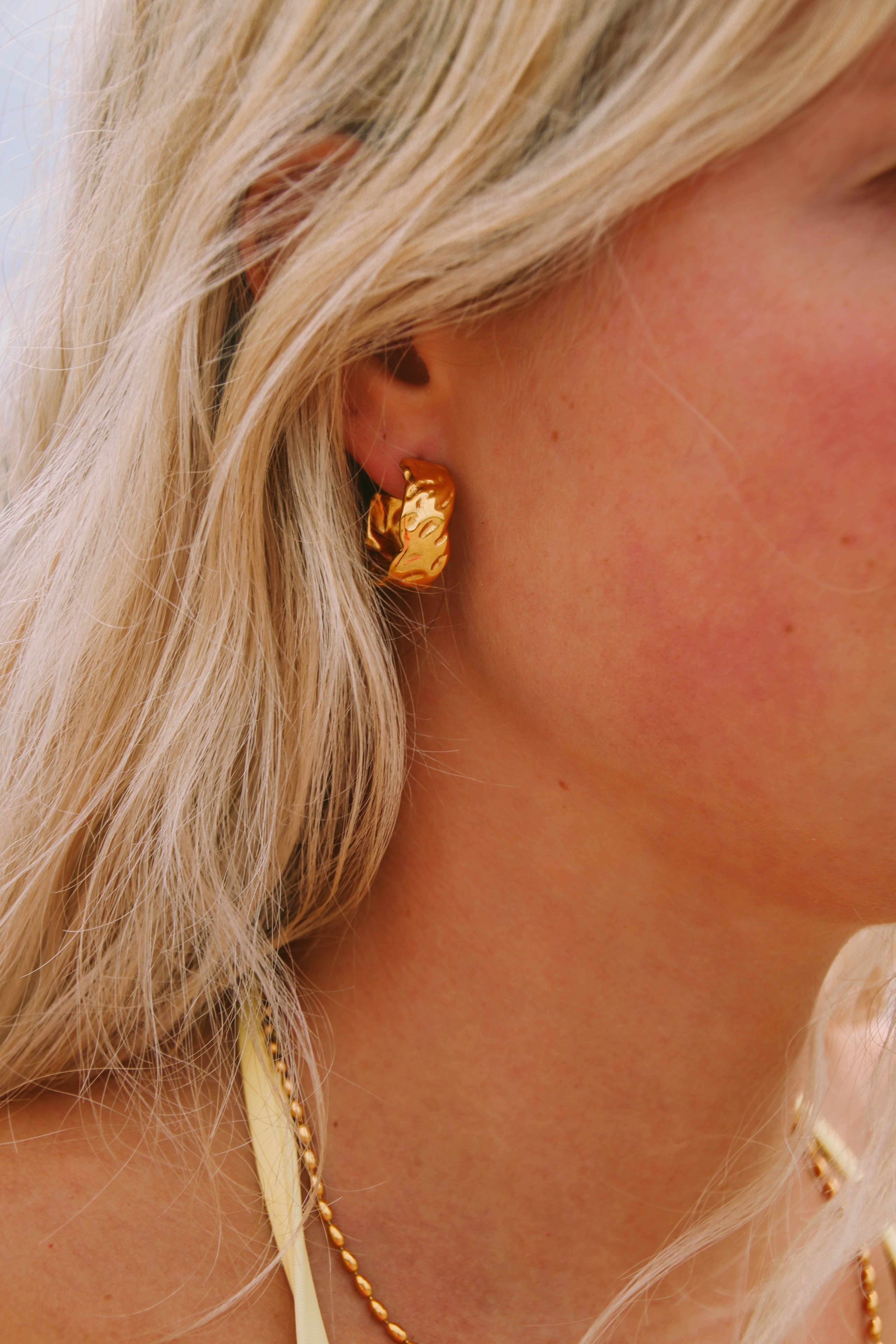 Närbild på Marigold Chunky Hoops från Alora Avenue – unika, organiskt formade guldörhängen som lyfter varje look. Vattentåliga och allergivänliga smycken, perfekta för både strand och fest.
