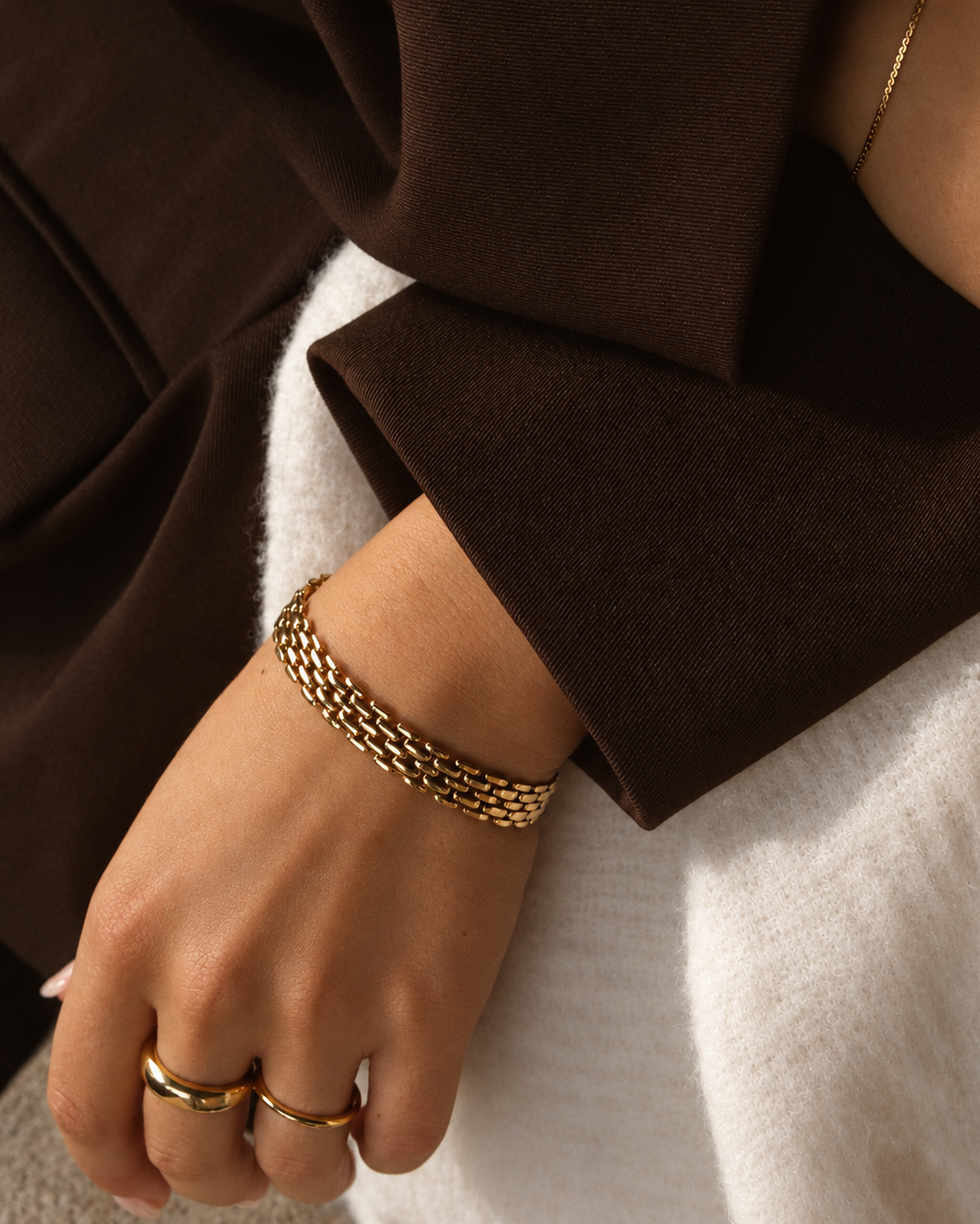 Maya Magnolia Bracelet i guld buret på modell till brun stickad ärm, stylat med guldringar. Vattentåligt och allergivänligt armband i rostfritt stål med 18K PVD-guldplätering från Alora Avenue.