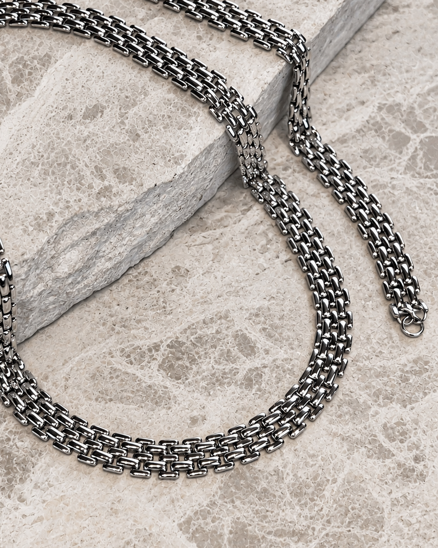 Millie Magnolia Necklace i silver fotograferat på marmor – brett, flätat bricklänkshalsband (panterlänk) med blank yta. Vattentåligt och allergivänligt halsband i rostfritt stål från Alora Avenue.