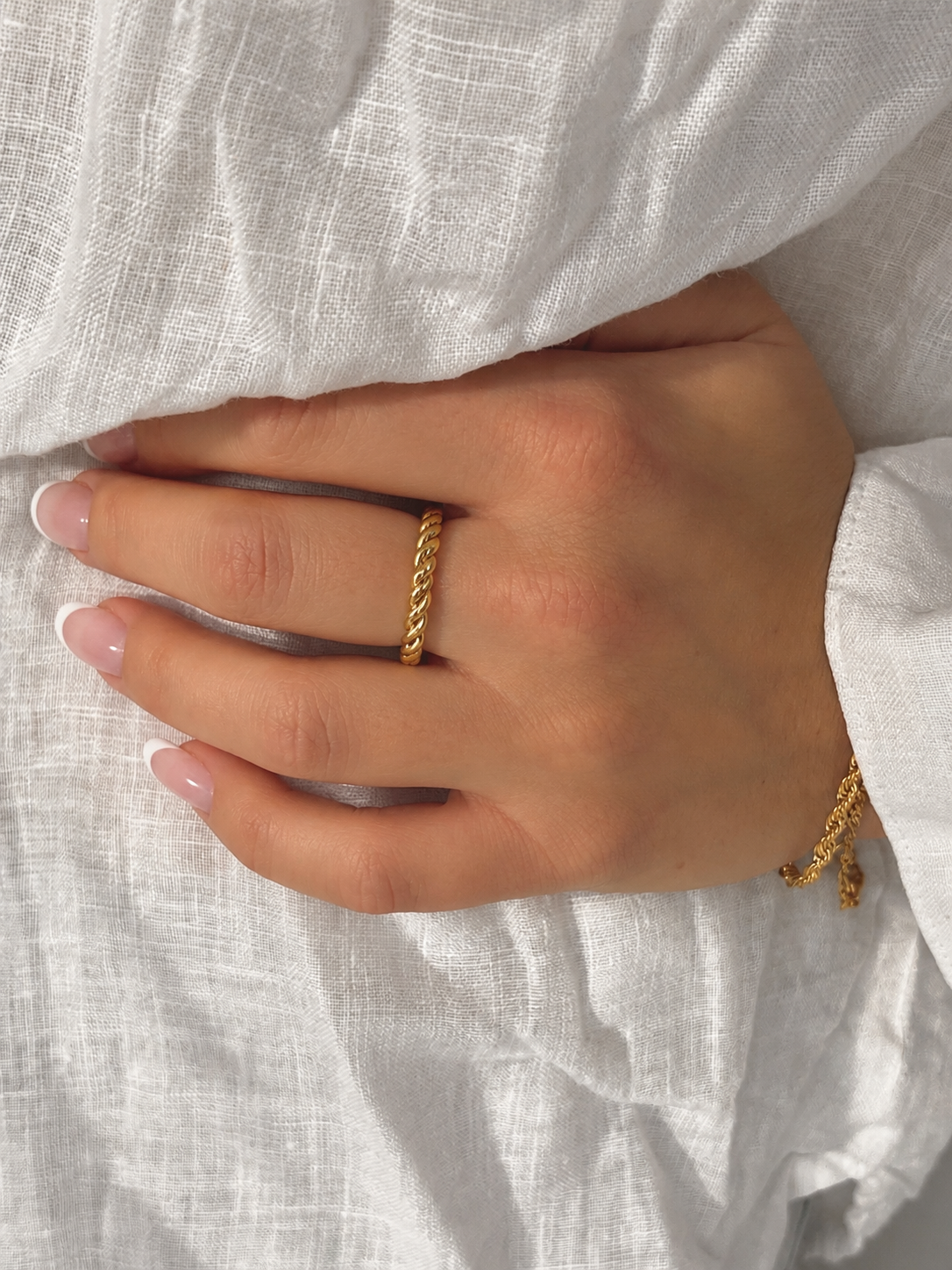 Minnie Moon Ring i guld på modell mot vitt linne – smal tvinnad ring. Vattentålig och allergivänlig ring i rostfritt stål med 18K PVD-guldplätering från Alora Avenue.