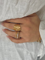 Minnie Moon Ring från Alora Avenue, staplad med andra guldfärgade ringar. Den tvinnade designen skapar en elegant struktur mot den vita linneskjortan.
