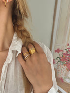 Minnie Moon Ring från Alora Avenue, stylad i en stack tillsammans med andra guldringar. En tunn, tvinnad guldfärgad ring som ger en sofistikerad och lekfull look.