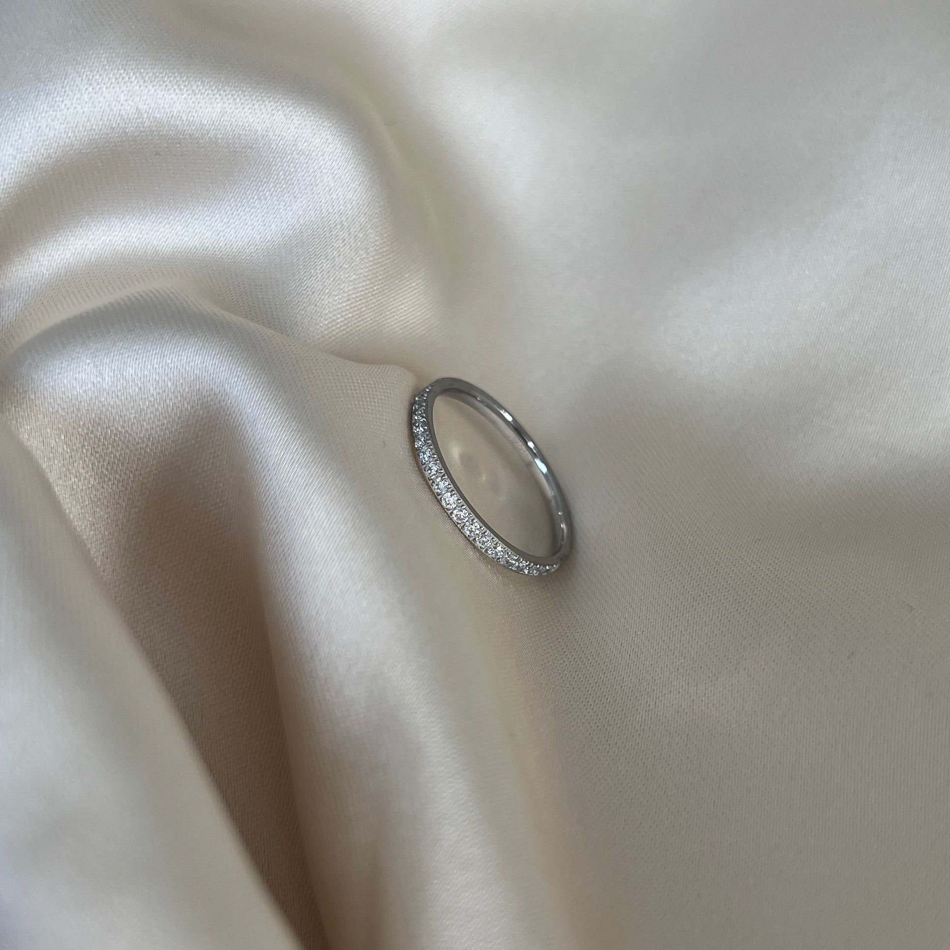 Noelle Glow Ring i silver med gnistrande stenar längs halva ringen, fotograferad på ljus sidenbakgrund. Tidlös, vattentålig och allergivänlig ring från Alora Avenue.