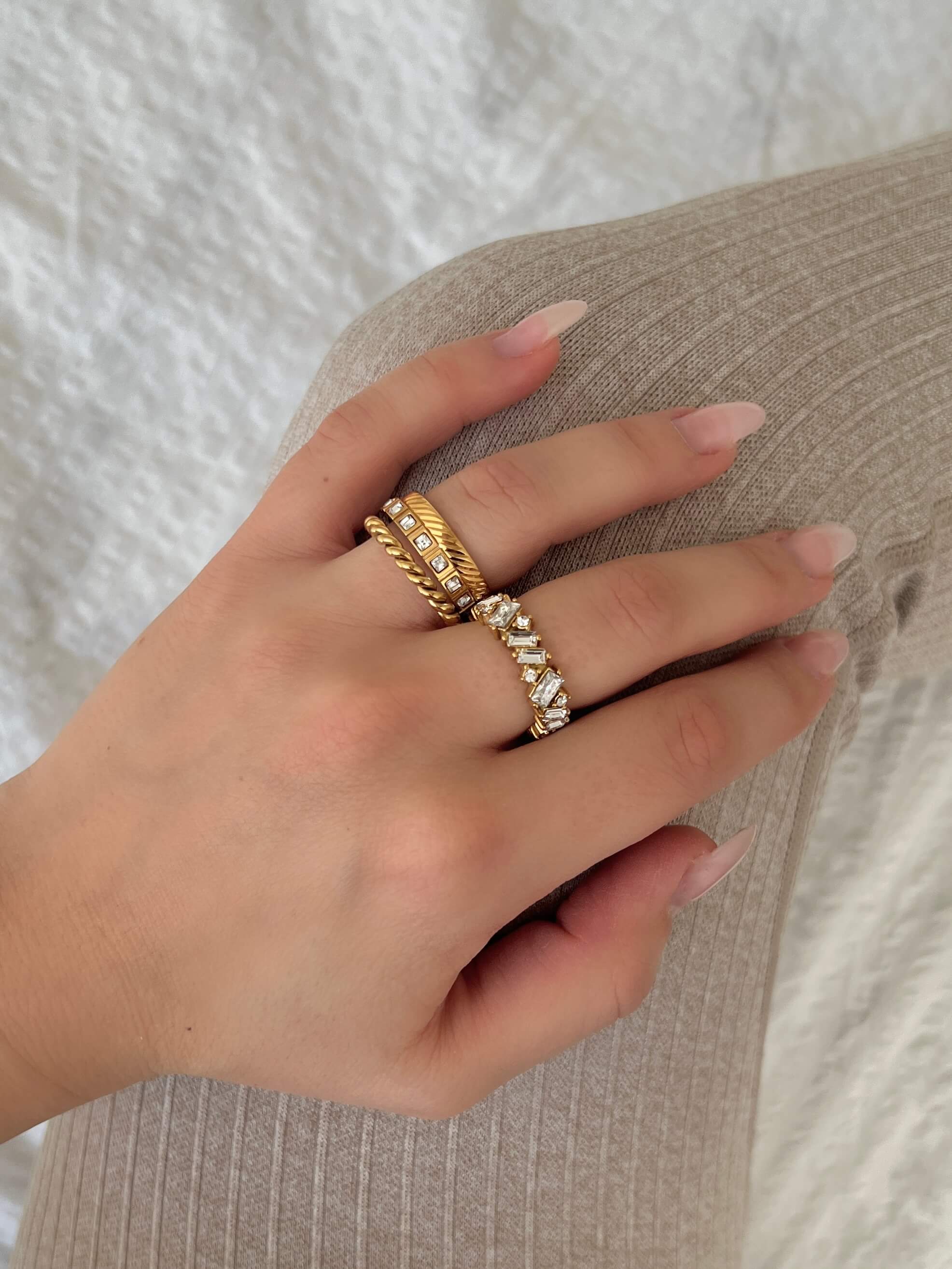 Oblique Olga Ring – tunn, guldfärgad ring med snedräfflad yta från Alora Avenue. Kombinerad med andra ringar för en stilsäker look. Vattentålig och allergivänlig – perfekt för vardag och fest.