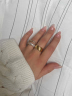 Oblique Orion Ring från Alora Avenue – en bred och elegant guldfärgad ring med snedräfflad yta, fångad i ett mjukt och mysigt ljus. Perfekt som en iögonfallande statementring.