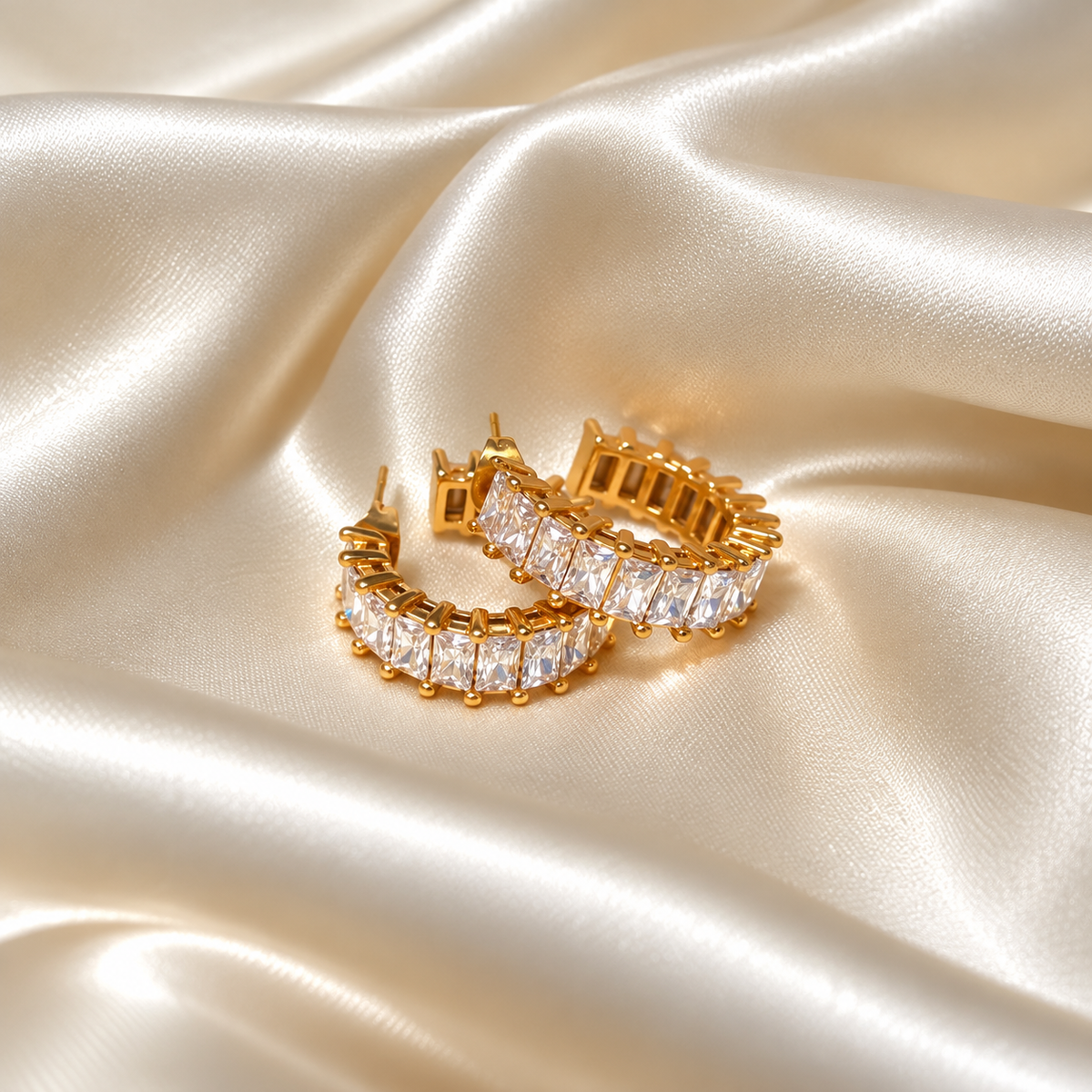 Sabrina Spark Hoops i guld fotograferad på ljust silkestyg. Vattentåligt och allergivänligt smycke i rostfritt stål med 18K PVD-guldplätering från Alora Avenue.