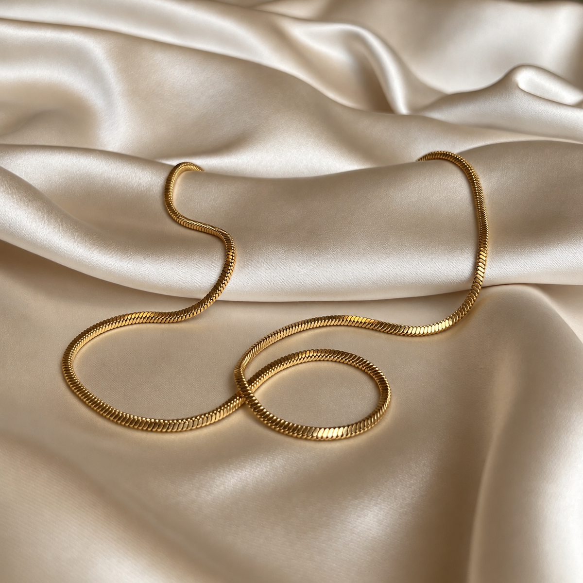 Sally Serpent Necklace i guld fotograferat på ljust silkestyg. Vattentåligt och allergivänligt halsband i rostfritt stål med 18K PVD-guldplätering från Alora Avenue.