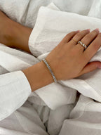 Närbild på Santiago Sunstone Bracelet från Alora Avenue – ett elegant tennisarmband med baguetteslipade kristaller, stylat med vita linnelakan och guldringar.