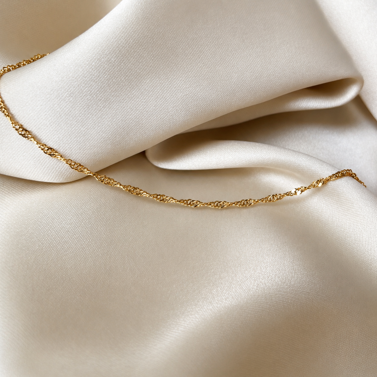 Sia Singapore Bracelet i guld fotograferat på ljust silkestyg. Vattentåligt och allergivänligt armband i rostfritt stål med 18K PVD-guldplätering från Alora Avenue.