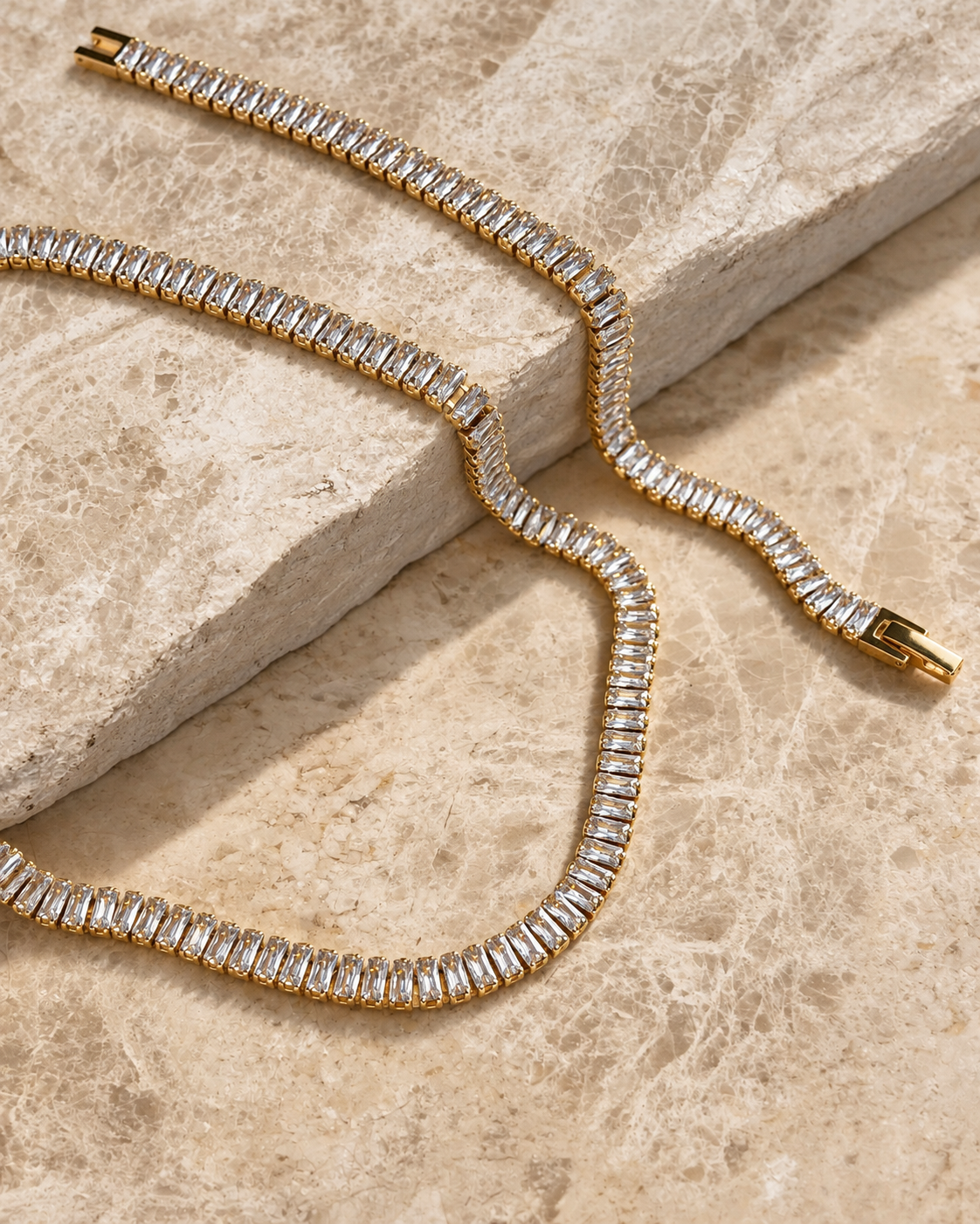Sienna Sunstone Necklace i guld fotograferat på travertin – tennishalsband med en rad baguetteslipade vita stenar i guldinfattning. Vattentåligt och allergivänligt halsband i rostfritt stål med 18K PVD-guldplätering från Alora Avenue.