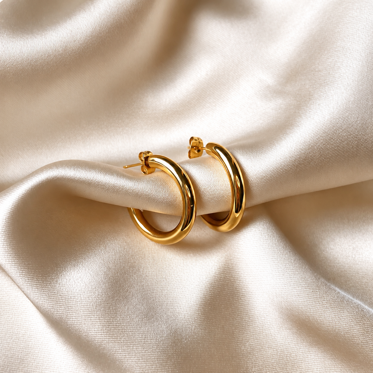 Simple Florence Hoops i guld fotograferade på ljust silkestyg. Vattentåliga och allergivänliga örhängen i rostfritt stål med 18K PVD-guldplätering från Alora Avenue.