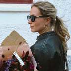 Sky Saturn Hoops i guld burna av kvinna i skinnjacka med blombukett. Stora, eleganta hoops från Alora Avenue – vattentåliga och perfekta för vardag och fest.