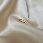 Solo Dazzle Ring på champagnefärgad siden – minimalistisk tunn guldfärgad ring med en liten klar sten. Vattentålig och allergivänlig, tillverkad i rostfritt stål med hållbar PVD-plätering. Perfekt för diskret vardagslyx eller att kombinera i en ringstack.