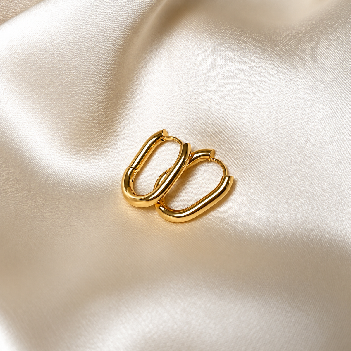 Stellar Serenity Hoops i guld fotograferade på ljust silkestyg. Vattentåliga och allergivänliga örhängen i rostfritt stål med 18K PVD-guldplätering från Alora Avenue.