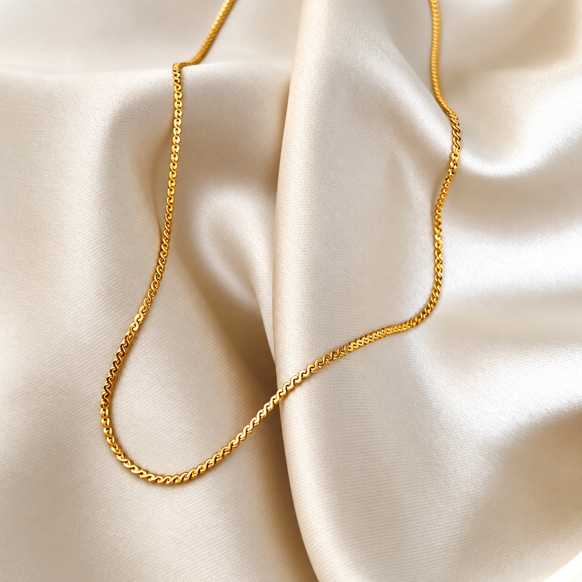 Svea Saffron Necklace i guld fotograferat på ljust silkestyg. Vattentåligt och allergivänligt halsband i rostfritt stål med 18K PVD-guldplätering från Alora Avenue.