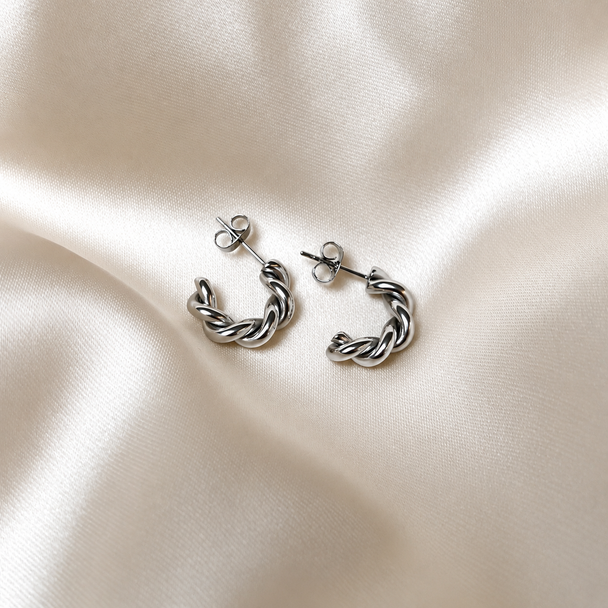 Tornado Edge Earrings i silver fotograferade på ljust silkestyg. Vattentåliga och allergivänliga örhängen i rostfritt stål från Alora Avenue.