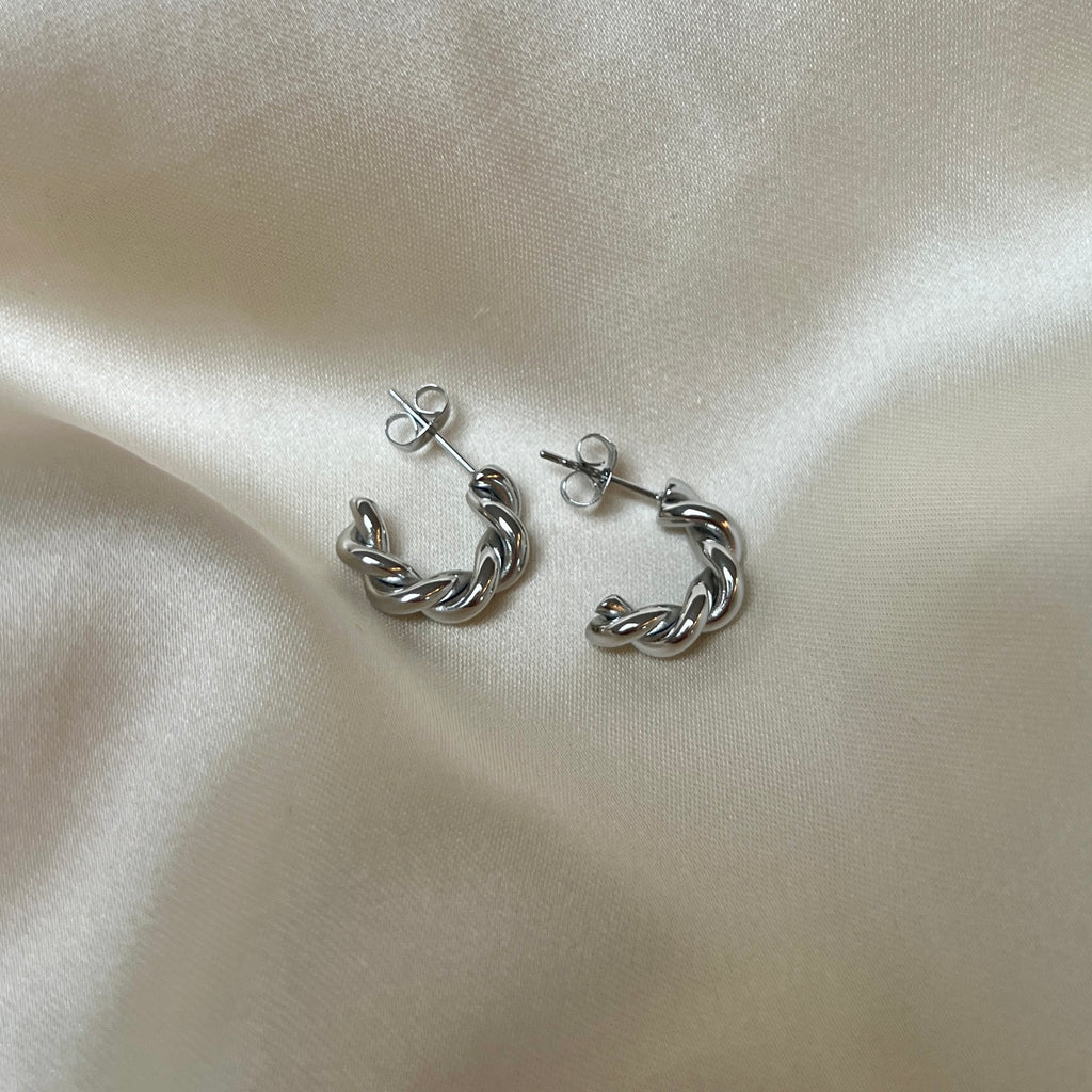 Tornado Edge Earrings – tvinnade silverörhängen i rostfritt stål från Alora Avenue. Fotade på mjuk sidenbakgrund. Vattentåliga, eleganta och perfekta för både vardag och fest.