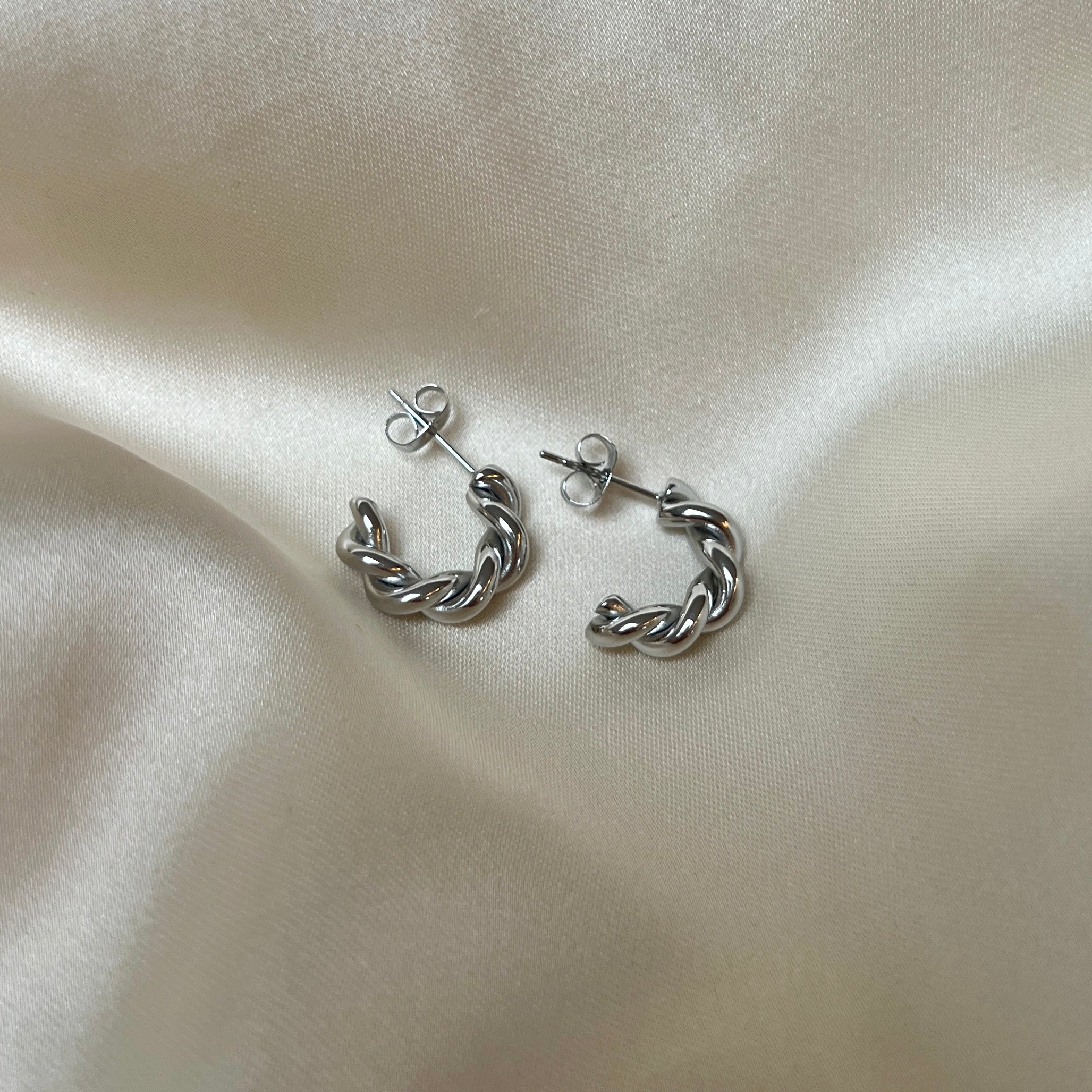 Tornado Edge Earrings – tvinnade silverörhängen i rostfritt stål från Alora Avenue. Fotade på mjuk sidenbakgrund. Vattentåliga, eleganta och perfekta för både vardag och fest.
