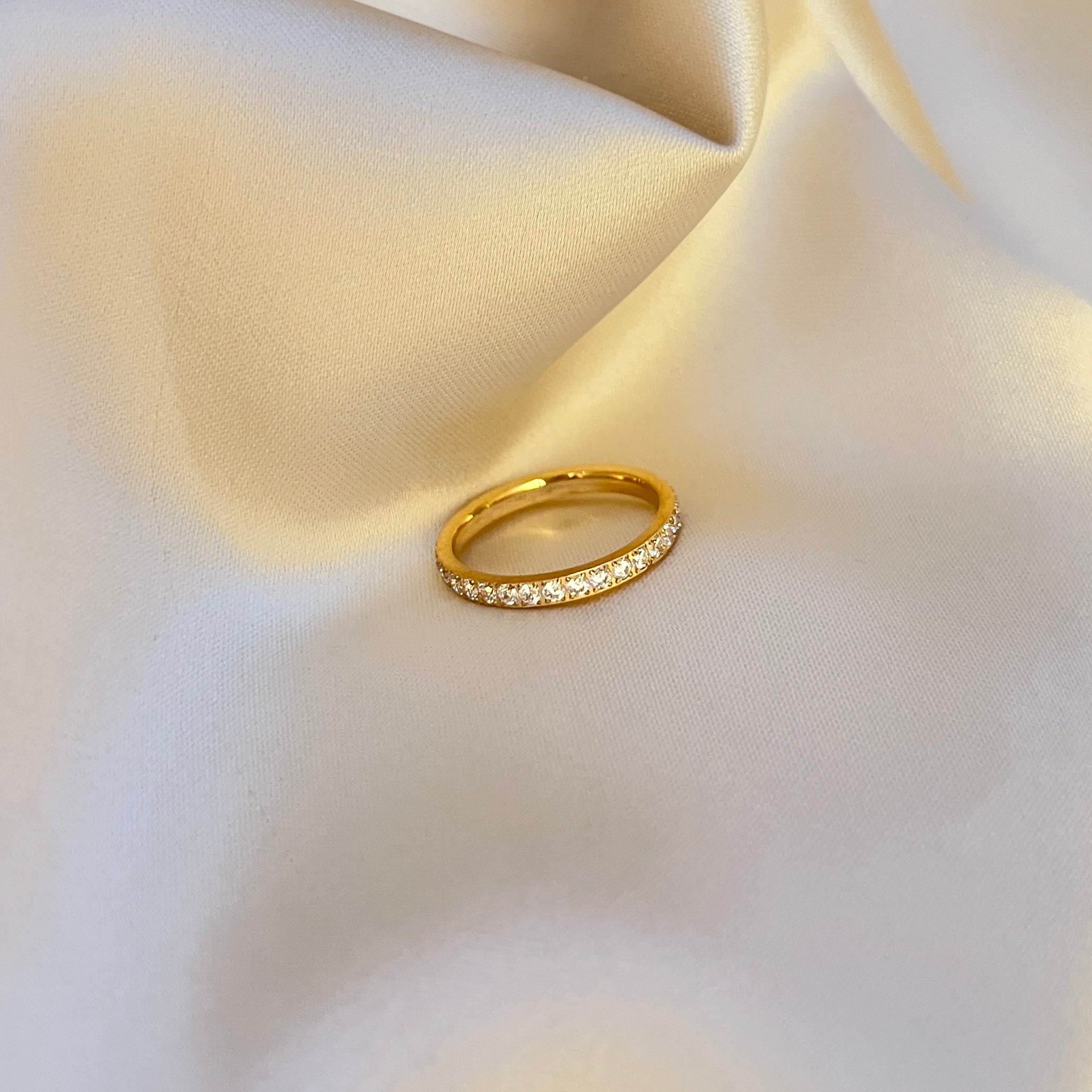 Twinkle Tara Ring – elegant guldfärgad ring med gnistrande stenar runt hela bandet. Perfekt att bära ensam eller kombinera med andra ringar. Vattentålig och allergivänlig – tillverkad i rostfritt stål med PVD-plätering för lång hållbarhet och glans.