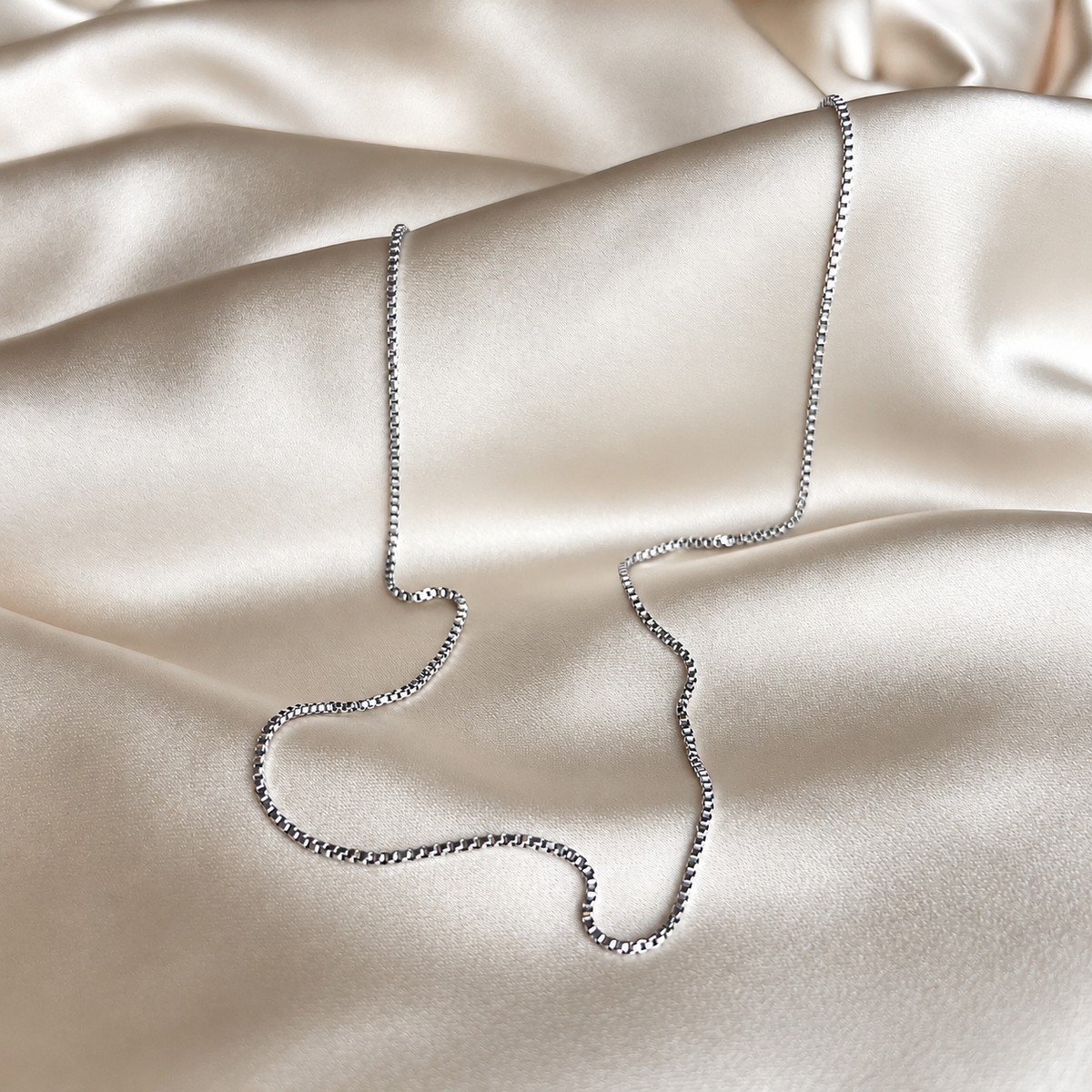 Vanessa Venezia Necklace i silver fotograferat på ljust silkestyg. Vattentåligt och allergivänligt halsband i rostfritt stål från Alora Avenue.